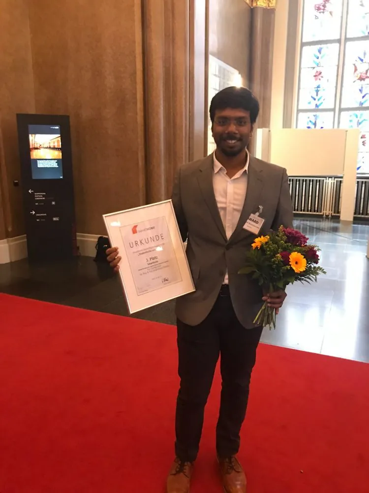 Anand Narasipuram holding the SmartHome Deutschland Award 2019 certificate for 3rd place, with a bouquet.
